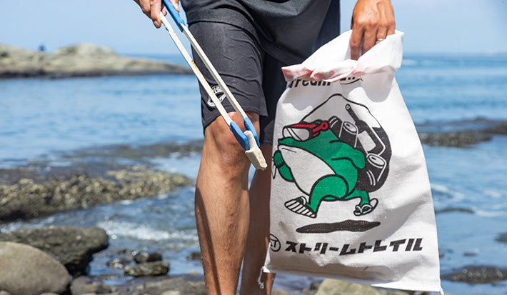 A close-up of a volunteer at the Enoshima Ocean Cleanup holding a trash bag and grabber.