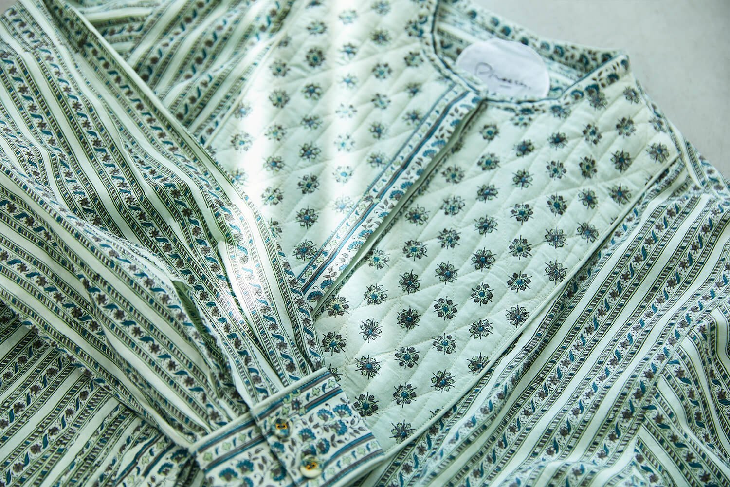 A close-up of a Pheeta quilted jacket with a floral block print, layered over a vertically striped shirt, showing the textile detail.